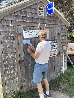 Nat Hussey posting flyer on shed door in Matinicus